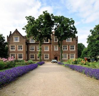 A beautiful gravel road surrounded by lavender bushes ate leading up to a large brick manor